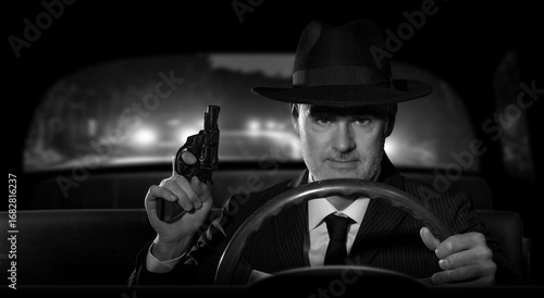 Εκτύπωση καμβά Detective with a gun in hand chasing criminals in his car, scene in 1950s American film noir style