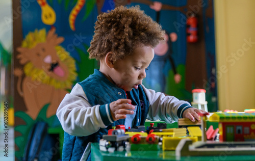 Toddler playing with a train set at nursery, kinder garden. Multi ethnic boy at playtime. 