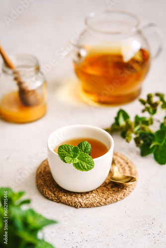 Pfefferminztee in einer Tasse und einer Glaskanne und Honig in einem Einmachglas auf einem weißen Tisch. Kräutermedizin, Teepause.