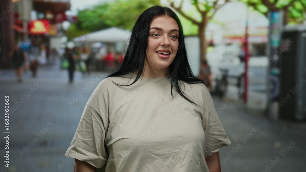 Fototapeta premium Woman smiling outdoors on a bustling city street with green trees in the background, embodying urban life and youthful energy in a casual beige outfit.