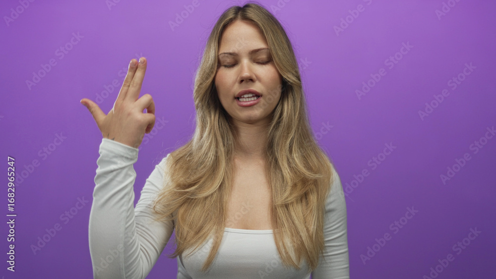 Fototapeta premium Blonde woman with long hair makes finger gun gesture with raised hand in purple studio setting; frustration sarcasm irritation.