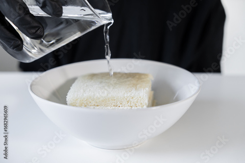 Cuadro en lienzo Person wearing black glove pours clear fresh water onto white toast bread slices