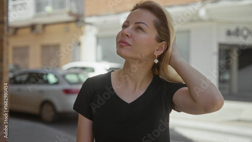 Free Download Young blonde woman covers mouth while yawning on midday sunny city street beside building facade; fatigue. - GFXLoad