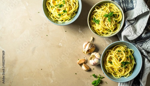 Three bowls of spaghetti with garlic and herbs are arranged on a marble surface, with a cloth napkin near. Overhead view with lots of copy space