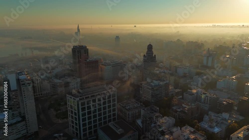 Drone view of sunrise in Montevideo, Uruguay, covered by fog. Buildings emerge faintly from the fog