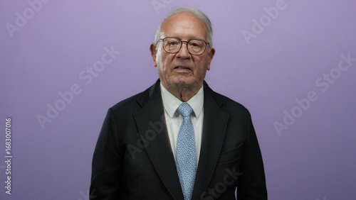 Photos Senior man in business suit points upward against an isolated purple background, conveying a thoughtful and professional expression