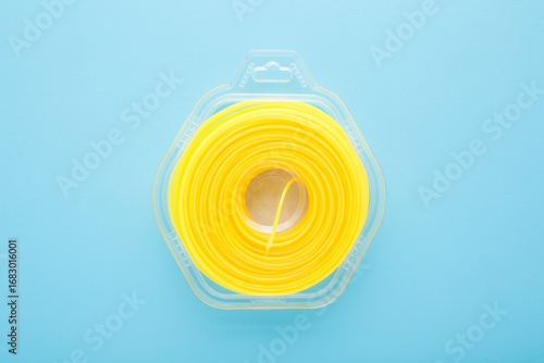 Fotografija New yellow trimmer line in transparent pack on light blue table background