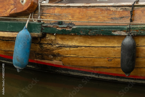 Billede på lærred Old wooden boat hull with fenders hanging showing signs of wear and tear