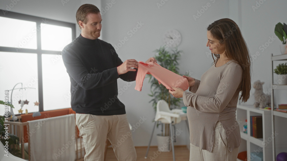 Obraz premium Pregnant woman and man prepare nursery in baby room with crib, displaying new pink baby clothes in a cozy home setting, emphasizing family bonding and anticipation.