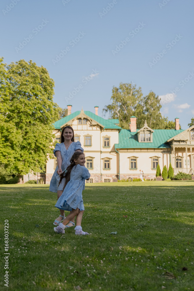 Obraz premium A happy woman and her daughter running through the grass in nature, with a wooden house in the background