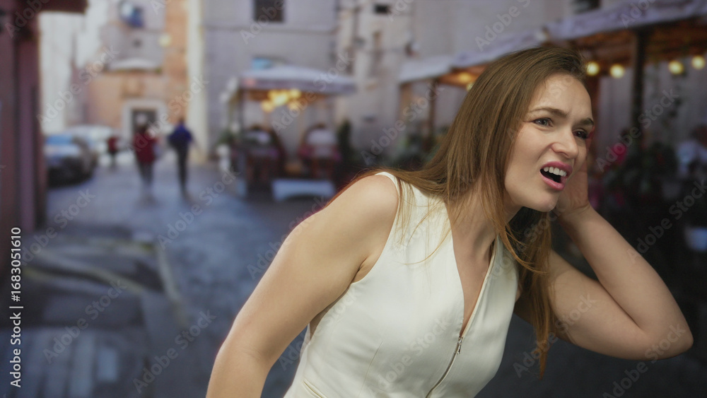 Fototapeta premium Woman holds hand to ear leaning forward and listening on a busy cobblestone street under evening light; confusion.