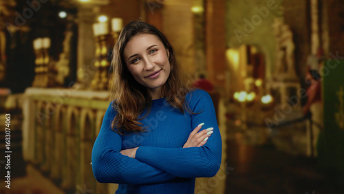 Wallpaper Mural Woman smiling indoors at church, wearing blue sweater, with folded arms and serene expression, surrounded by decorative candlesticks and warm lighting. Torontodigital.ca