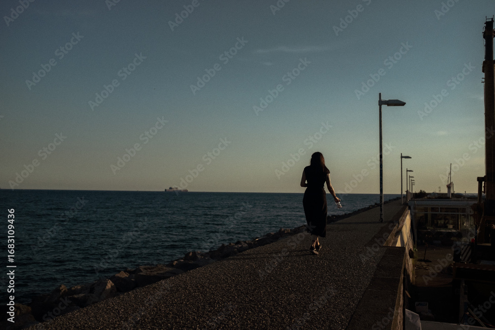 Fototapeta premium woman walking on the pier at sunset