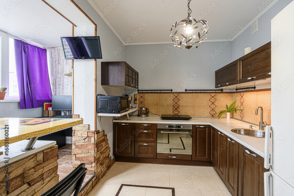 Fototapeta premium cozy kitchen with dark wood cabinets, light countertops, and tan tile backsplash. A unique light fixture hangs overhead