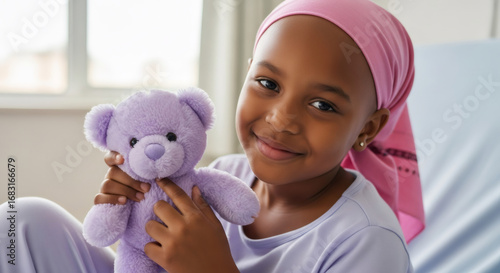 African american girl with pink scarf holding purple teddy bear. Child patient in hospital bed. Children healthcare and support concept.