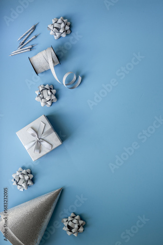 Holiday festive party flat lay with silver carnaval caps and cake candles, top view. Gift box and streamers on blue background