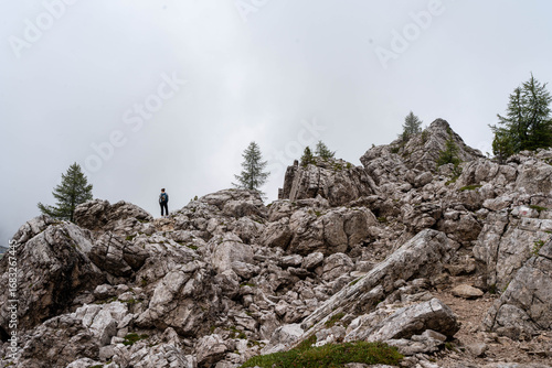 Lonely traveler standing on high mountain ridge surrounded by rocky terrain