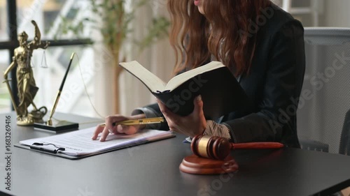 woman is sitting at a desk with a book and a pen. She is reading the book and she is focused on the content