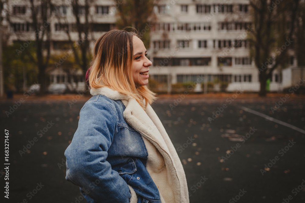 Fototapeta premium A young woman explores an urban park during an overcast day, surrounded by towering buildings and autumn foliage