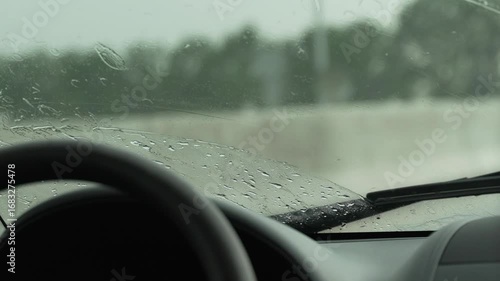 Rain Car Windshield: Rainy day view, wipers moving, water droplets obscure outside view.