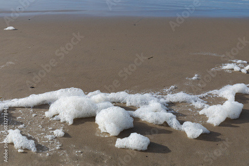 Mounds of sea foam on a sandy beach at the ocean's edge, environmental background, horizontal aspect