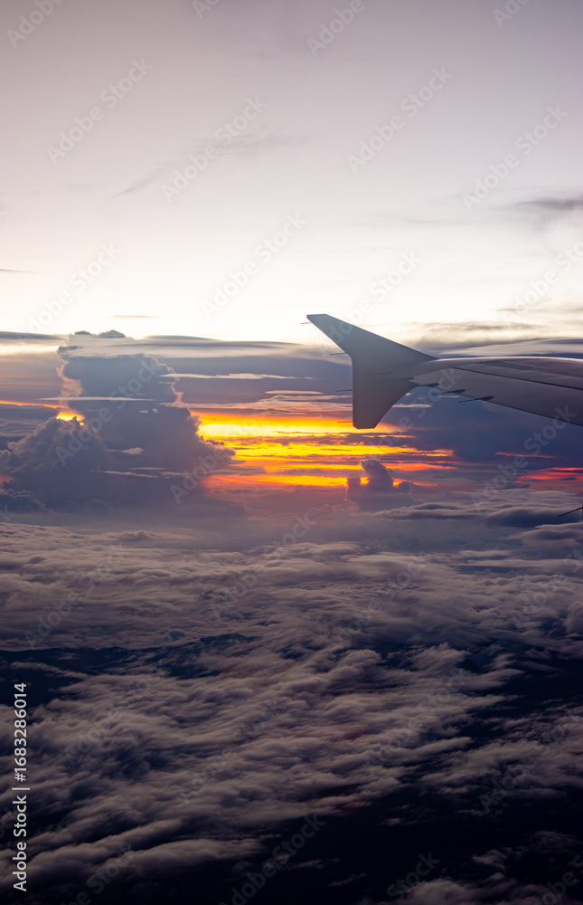 Fototapeta premium Scenic aerial view from an airplane wing capturing a vibrant sunset over the clouds, showcasing the beauty of travel and nature.