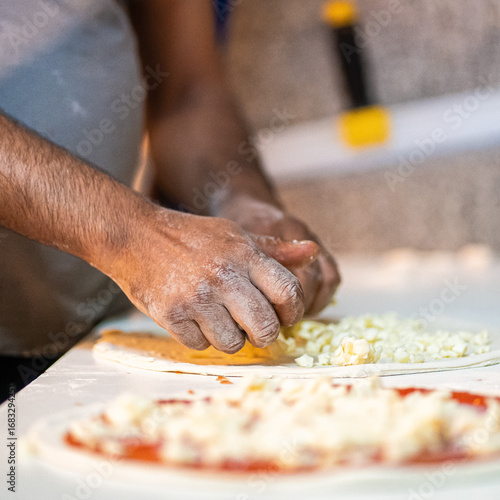 Hands preparing a pizza putting cheese mozzarella on pizza