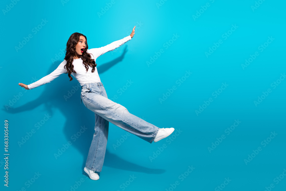 Obraz premium Stylish young woman posing excitedly in casual denim and white shirt against vibrant blue background