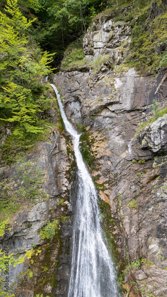 Obraz premium Aerial view of Sutovsky waterfall cascading through lush forest in Mala Fatra National Park, Slovakia. Majestic nature scene in Europe, perfect for travel, documentary and environmental projects