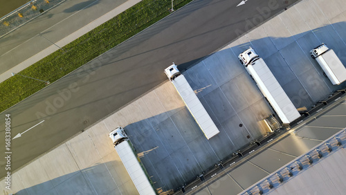 Aerial view of a logistics hub with four trucks at loading docks, showcasing efficient freight transportation and organized warehouse operations, highlighting modern logistics infrastructure.