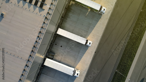 Aerial view of a distribution warehouse with three parked trucks, showcasing efficient freight logistics. Emphasizes organized cargo handling and industrial infrastructure.