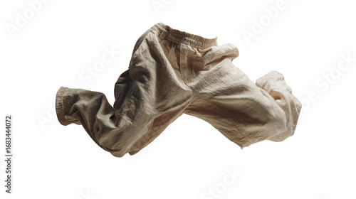 A pair of light beige linen pants, draped and floating against a black background.  The fabric appears soft and textured, with subtle folds and wrinkles.  The pants are isolated from the background