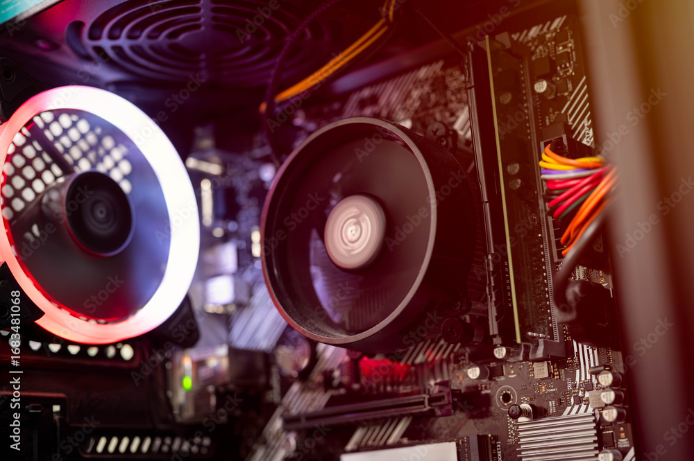 Fototapeta premium Close-up view of RGB cooling fan, CPU cooler, RAM, and colorful cables inside custom-built gaming PC with red-orange lighting. Ideal for illustrating modern computer hardware and build concepts.