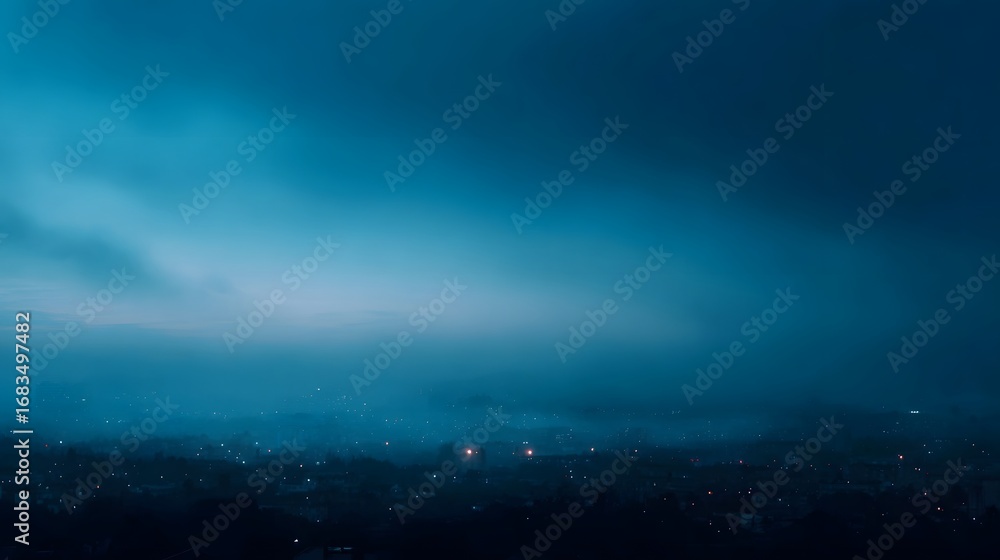 Naklejka premium Panoramic view of a city emerging from dense mist and fog at the tranquil blue hour with faint glowing lights illuminating the landscape