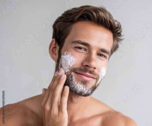 A man applies shaving cream to his face, displaying a gentle and approachable expression.