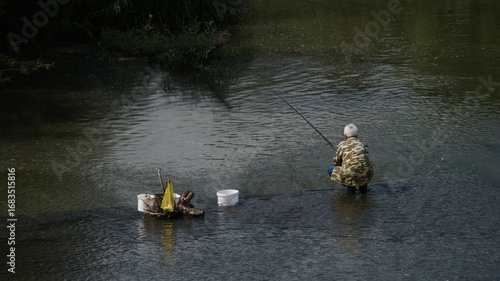 Fisherman in camouflage jacket sitting in river and fishing