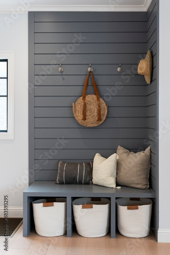 Chic blue paneled foyer with bench, cubbies and hooks, styled with pillows and straw bag and hat.
