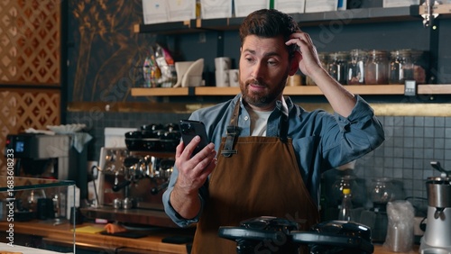 Photos Confused Caucasian barista employee guy waiter owner worker male man using mobil