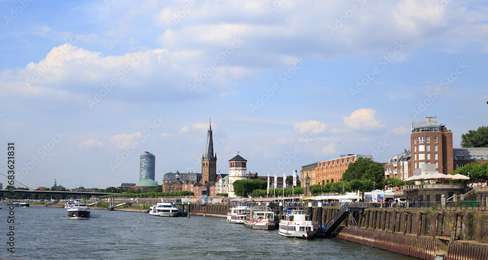 Fototapeta premium Dusseldorf , Germany. Busy port where tour boats and river cruise boats dock to allow passengers off to explore the City. St Lambertus Church is in the background