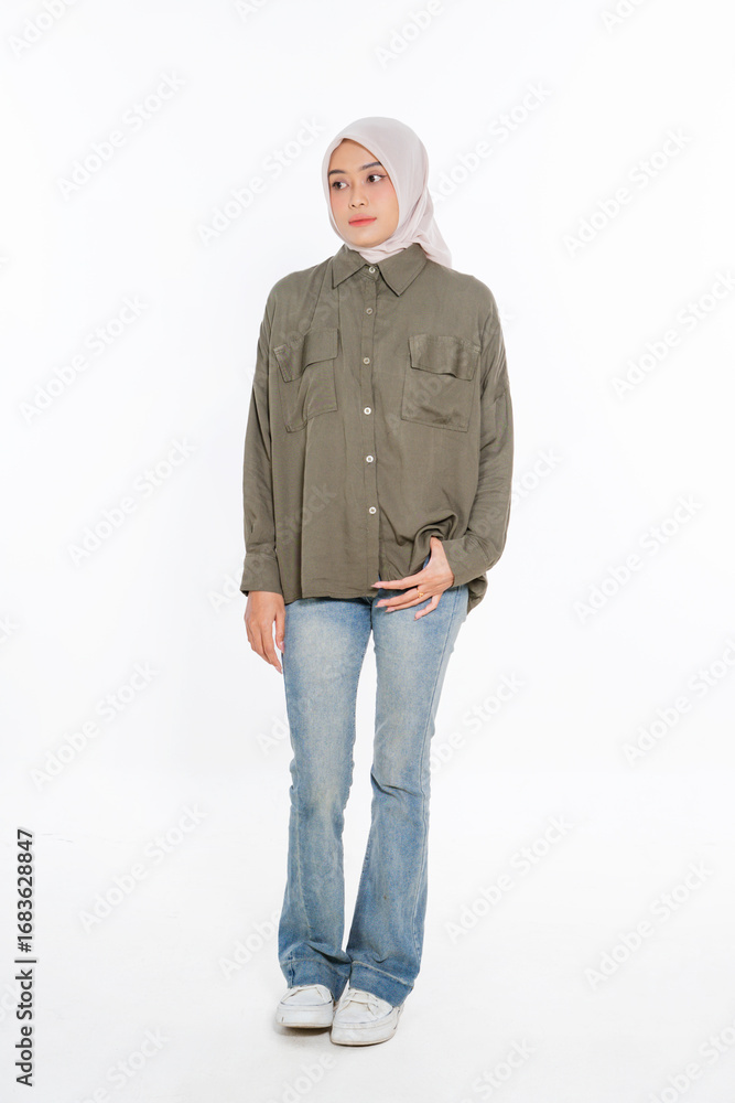 Fototapeta premium A stylish woman is dressed in an olive green shirt paired with jeans, complemented by a hijab