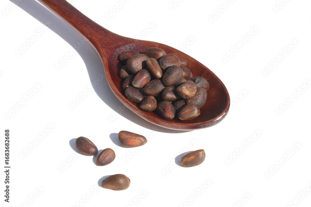 Fototapeta premium On a white background lies a wooden spoon with pine nuts. 