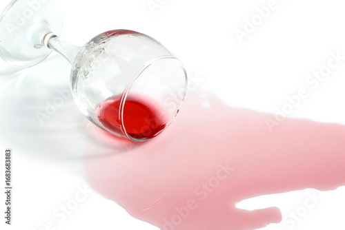 An overturned glass of red wine lies on a white background.
