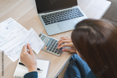 Tableau sur toile Stressed asian young business woman, employee using calculator to calculate expenses of monthly, hand holding bills and receipt for to payment on table at home