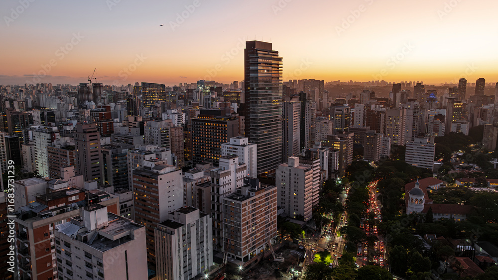 Fototapeta premium Drone aerial view of São Paulo city skyline at sunset over Avenida 9 de Julho with illuminated skyscrapers, residential buildings, heavy traffic and twilight sky in Brazil