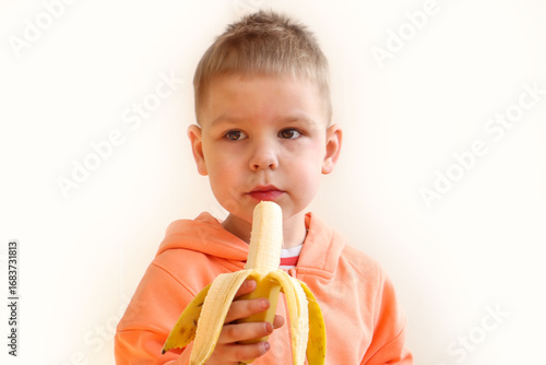 Three year old boy eats banana on light background