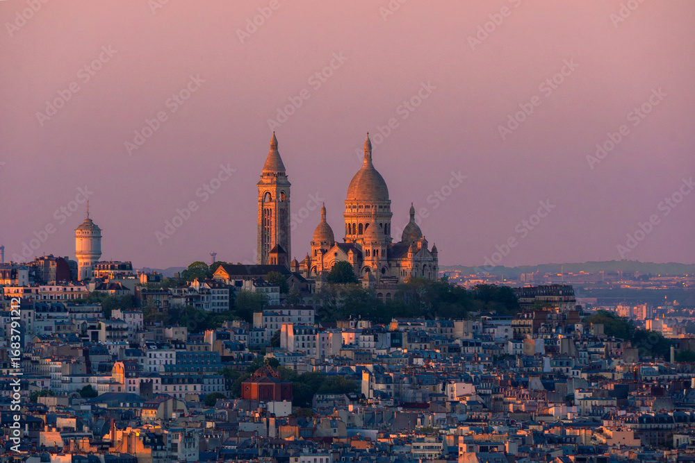 Fototapeta premium Panoramic aerial view of the Basilica of the Sacred Heart in Montmartre beautifully illuminated by the last lights of the sunset, under a purple sky in Paris, France.