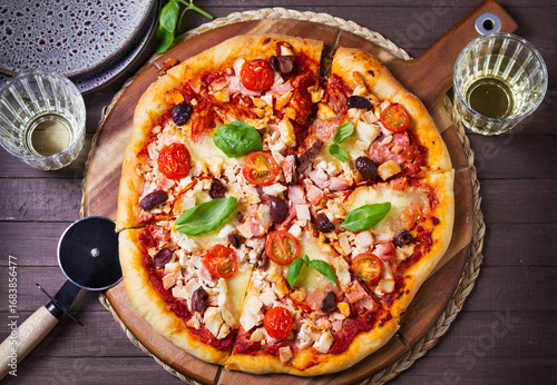 Delicious pizza served on wooden pizza board on brown background. View from above, top studio shot