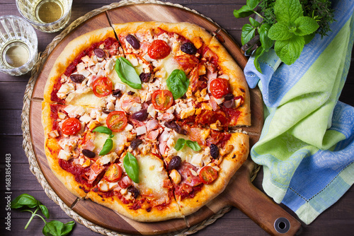 Delicious pizza served on wooden pizza board on brown background. View from above, top studio shot
