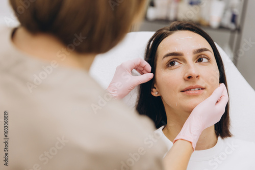Bild auf Leinwand Cosmetologist marking woman's face before cosmetic injections in clinic