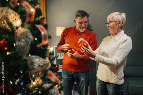Fotografie Senior couple decorating christmas tree with red ornaments